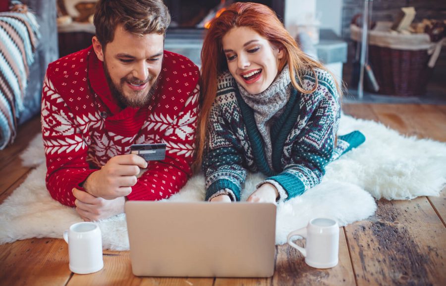 Happy couple in Christmas sweaters shopping online on laptop.