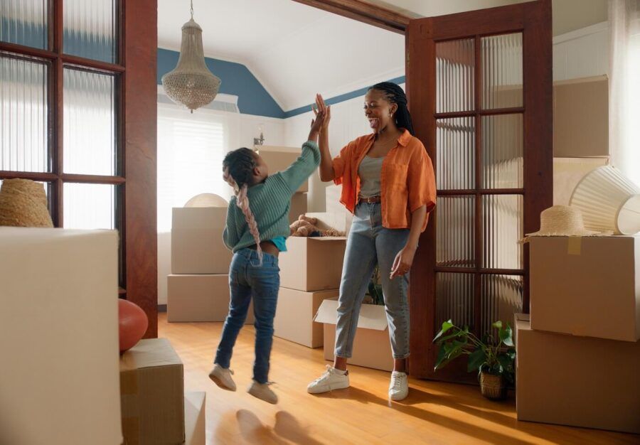 Smiling mother and young daughter share a joyful high five in their new living room, surrounded by unpacked moving boxes