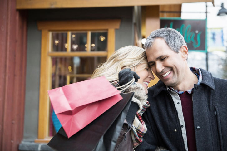 Laughing couple with shopping bags hugging outside storefront