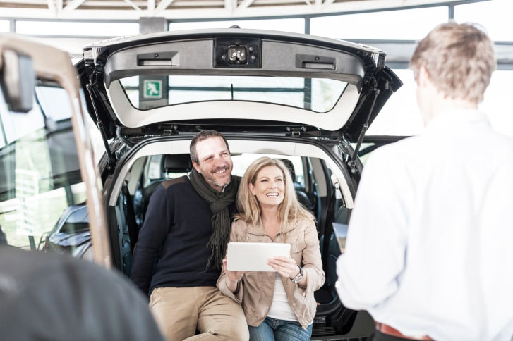 Smiling couple sitting in boot of new car at car dealership
