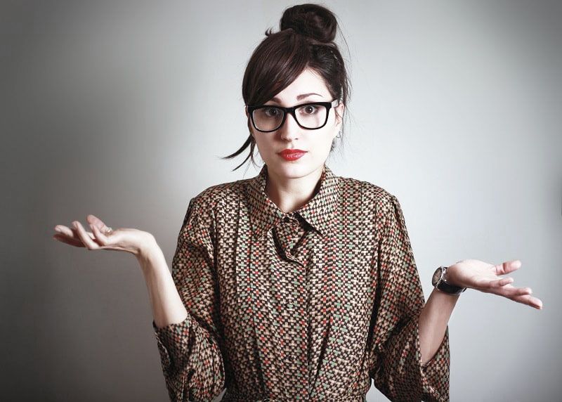 woman with black glasses and ponytail in patterned shirt against dark background