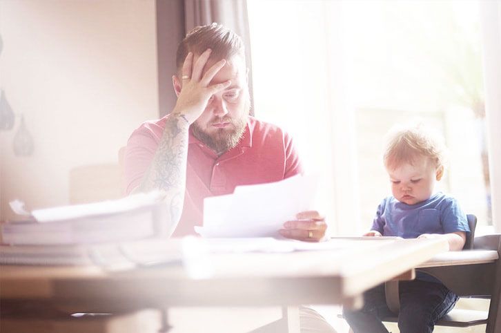 worried looking man pouring over finances sitting next to small child