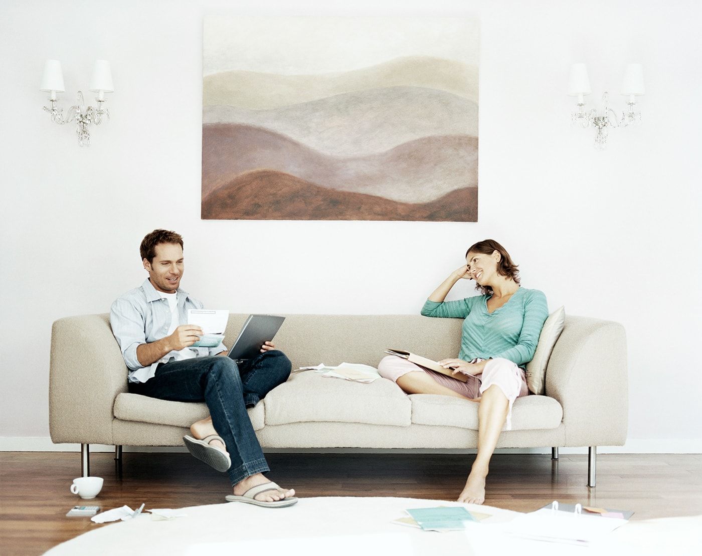 A man and a woman sitting on opposite ends of a couch, each holding financial papers.