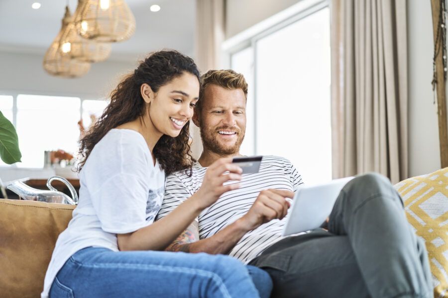 Smiling woman sitting with credit card next to a man who is paying via tablet at home