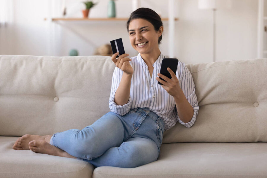 smiling woman sitting on couch holding credit card