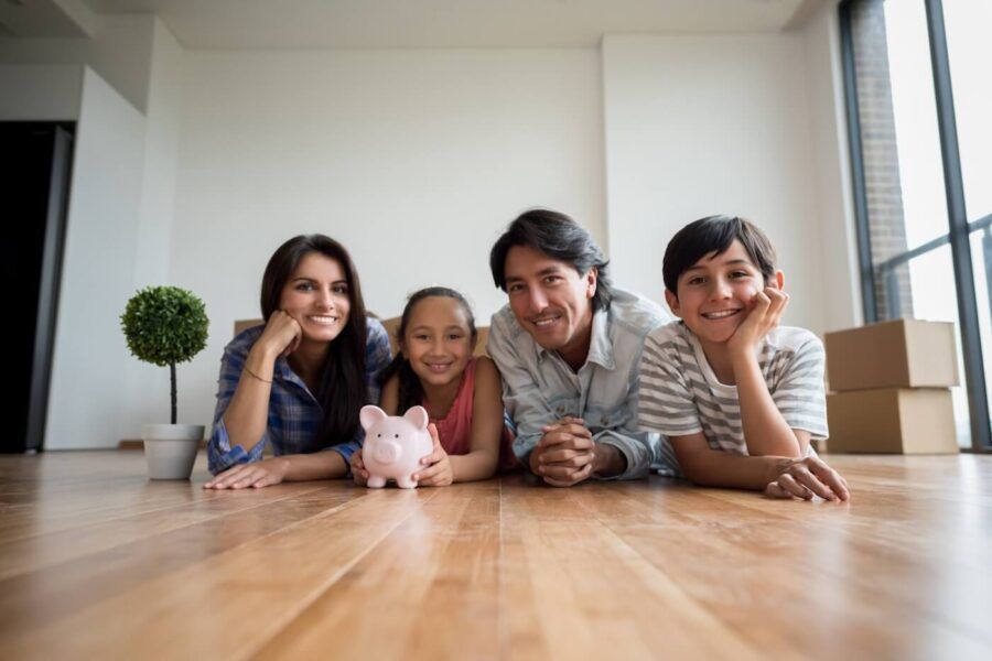 Happy family of four posing for a photo on the floor, the girl is holding a piggy bank