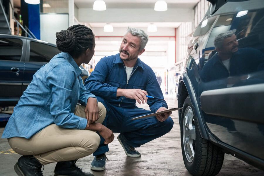A car mechanic talks with a customer next to their car while at the auto repair shop.