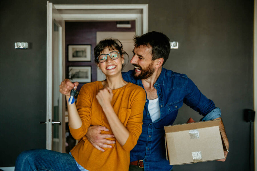 A couple smile and embrace each other while the woman holds the keys to the home.