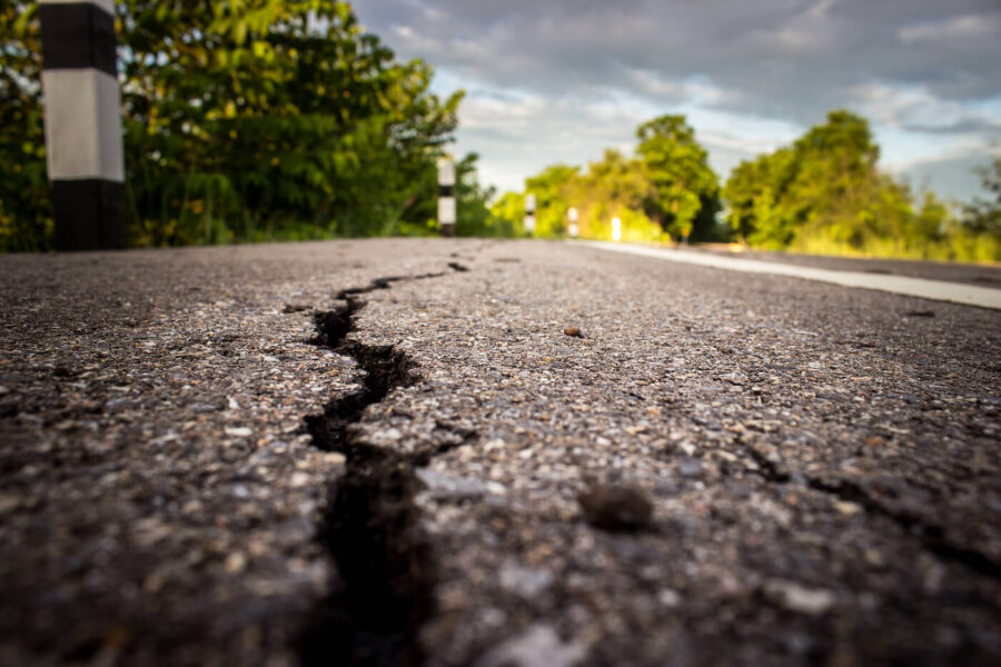 A large crack is next to the road with trees in the background.