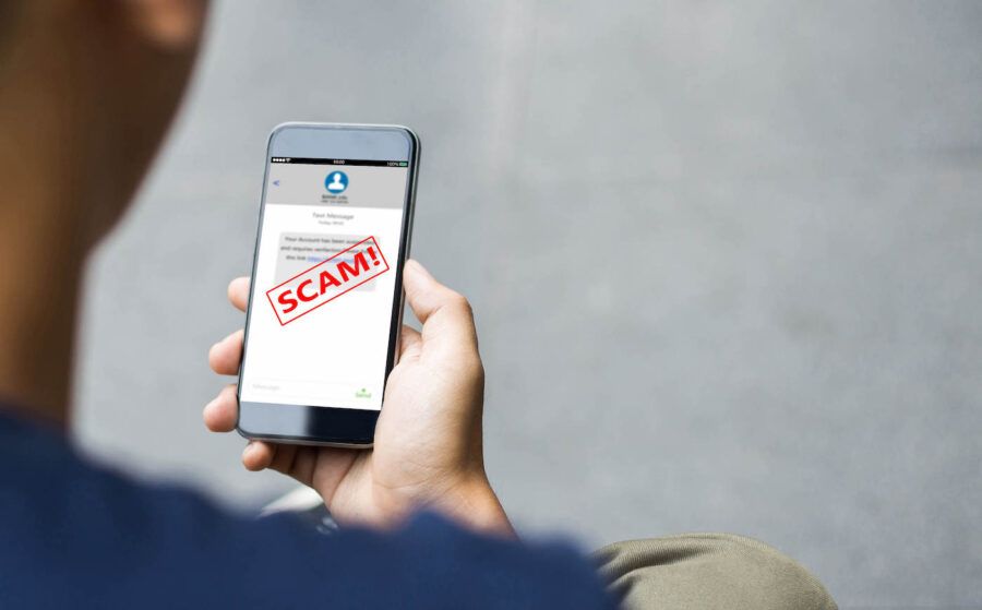A man holding his phone is looking at a text message with a scam alert.