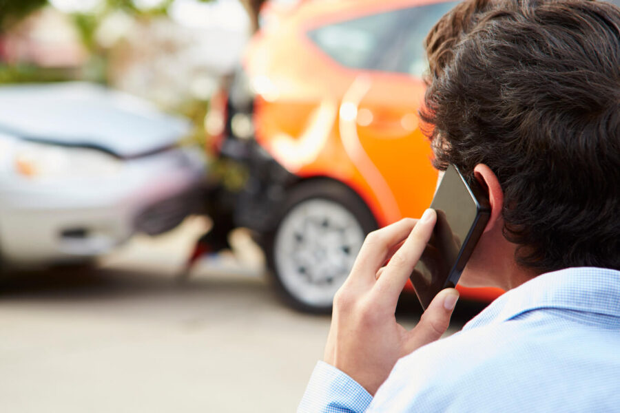 A man has his phone to his ear while looking at a car accident.