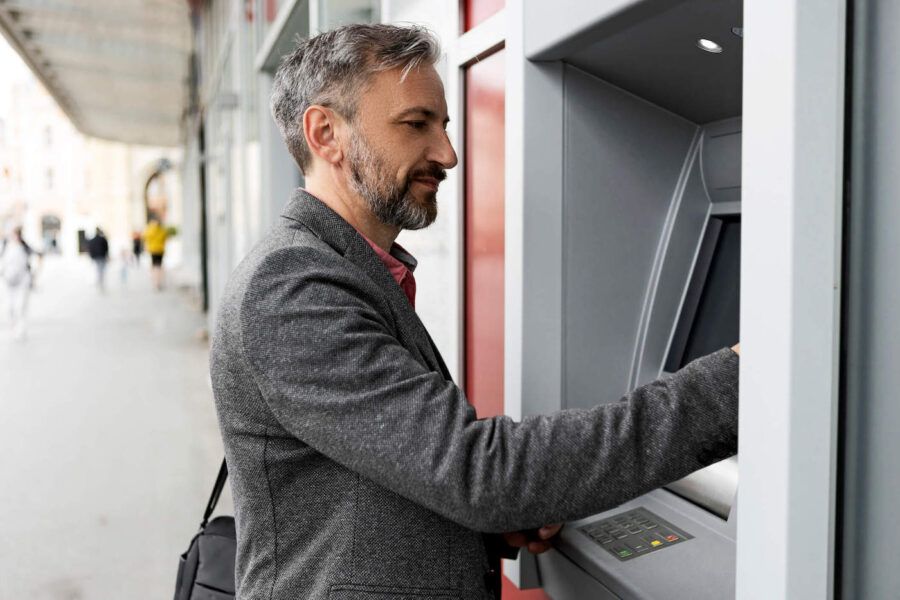 A man wearing a gray suit is using the ATM in the street.