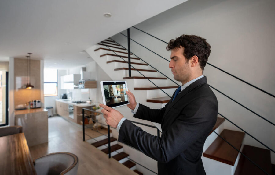 A man wearing a black suit takes a picture of a home using a tablet.
