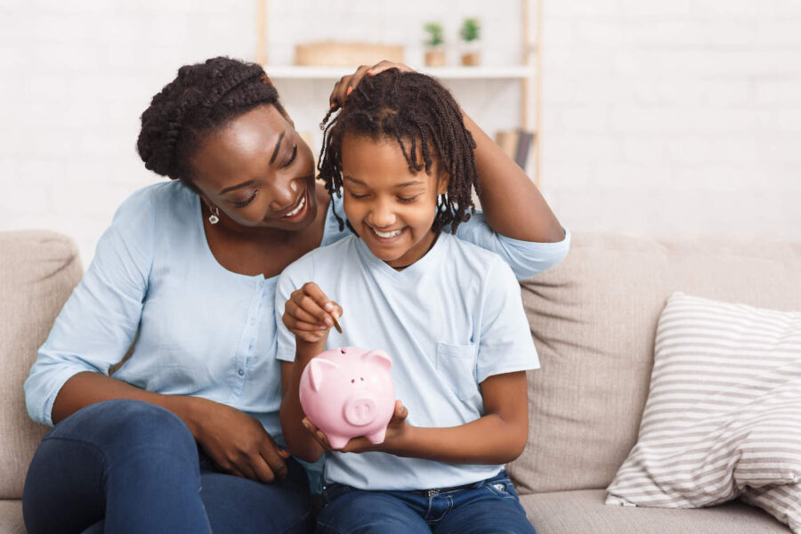 A mother and son smile together while putting money inside a piggy bank.