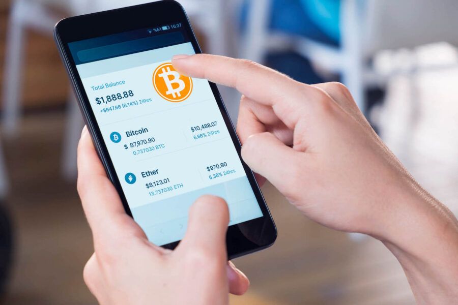 A hand clicks a bitcoin sign on their phone while it shows their crypto portfolio balance.