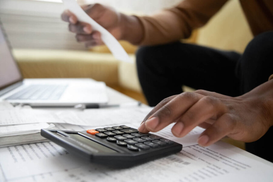 A person uses a calculator on top of documents while looking at a receipt next to their laptop.