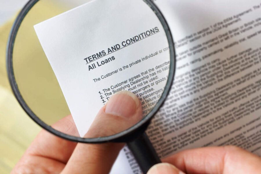 A person is holding up a magnifying glass to read the terms of a loan agreement.