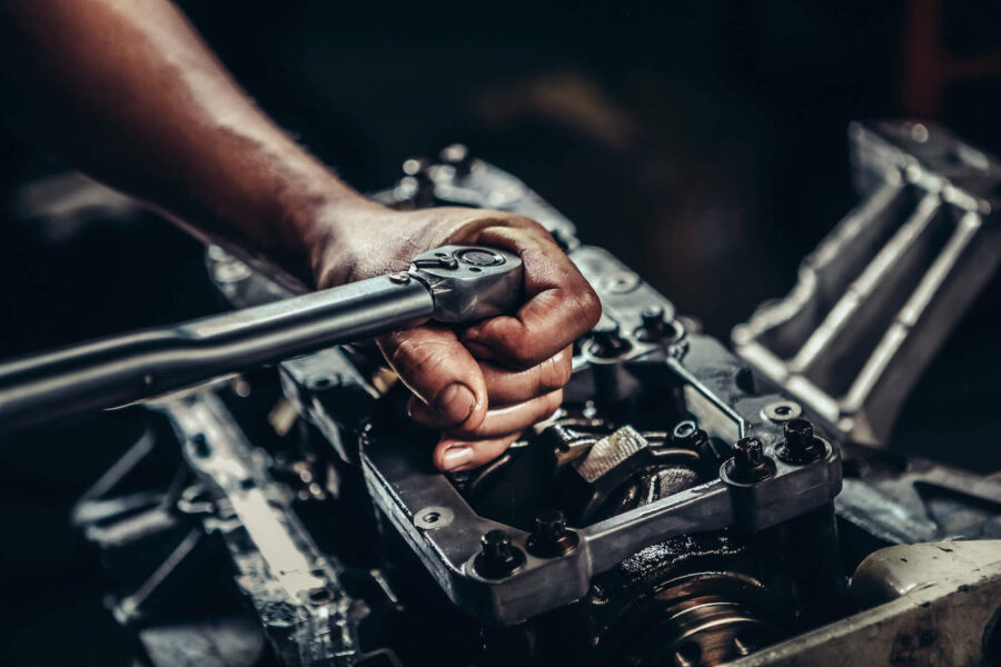 A person with dirt on their hands is tightening a bolt of a car engine using a torque wrench.