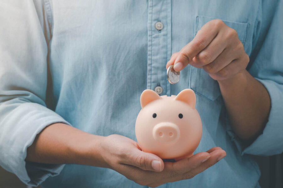 A person wearing a blue shirt is holding a pink piggy bank while putting a coin in.