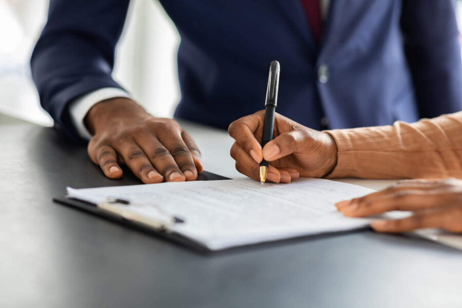 A person wearing a blue suit is handing over a document that another person is signing with a black pen.