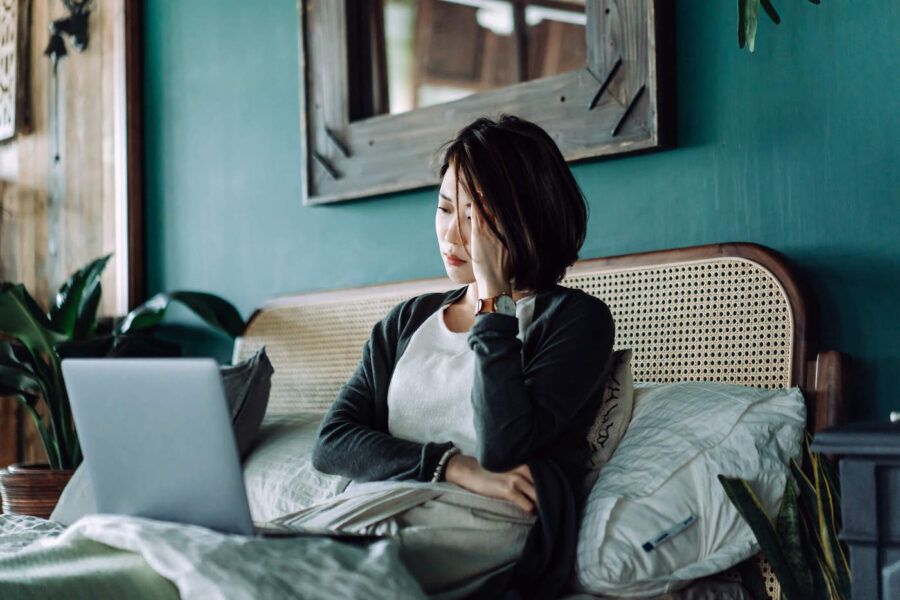 A woman frowns as she looks at her laptop while she lays down in bed.