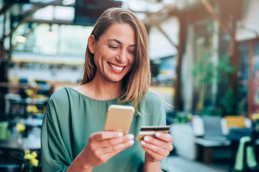 A Woman Smiles At Her Credit Card While Holding Her Phone