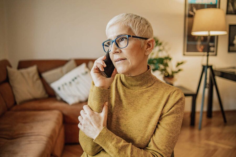 A women wearing a yellow sweater and black glasses is on the phone at her living room.