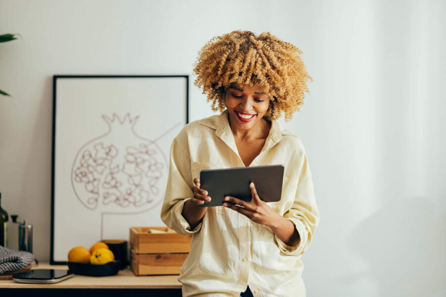 Afro-American Woman Standing and Smiling While Looking at a Digital Tablet.