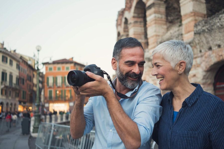 Older couple smiles at each other while the man holds a camera on their vacation.