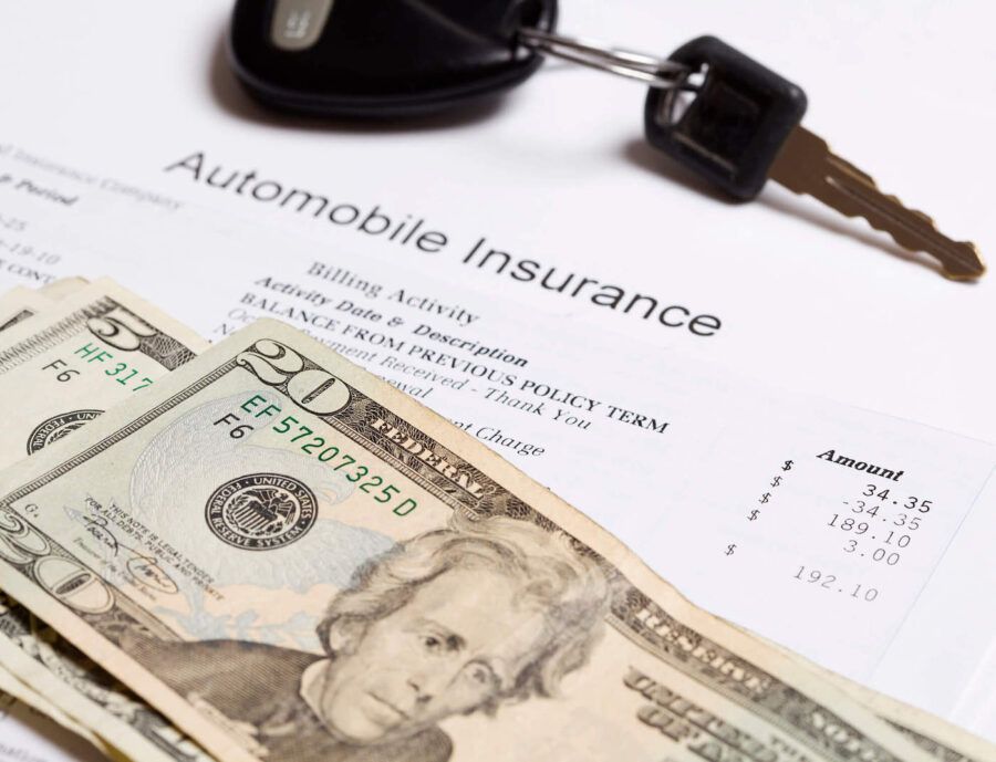 An automobile insurance document is under a stack of cash and a set of car keys.