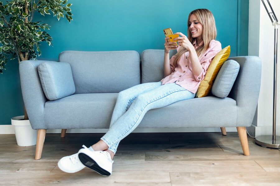 A woman sits on the couch while holding her credit card and phone.