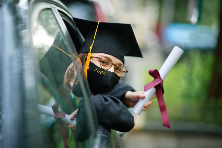Teenage girl wearing graduation gown and cap and protective mask with diploma in car