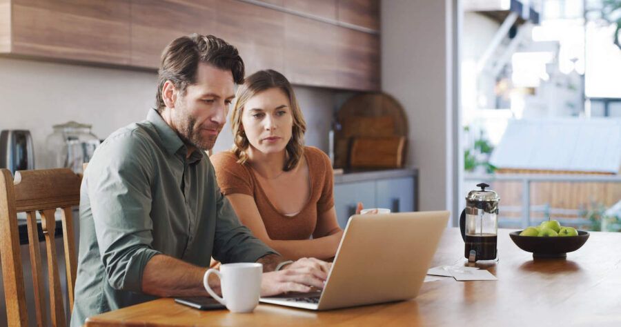 man and woman sitting on a wooden table renewing their term life insurance policy on a laptop