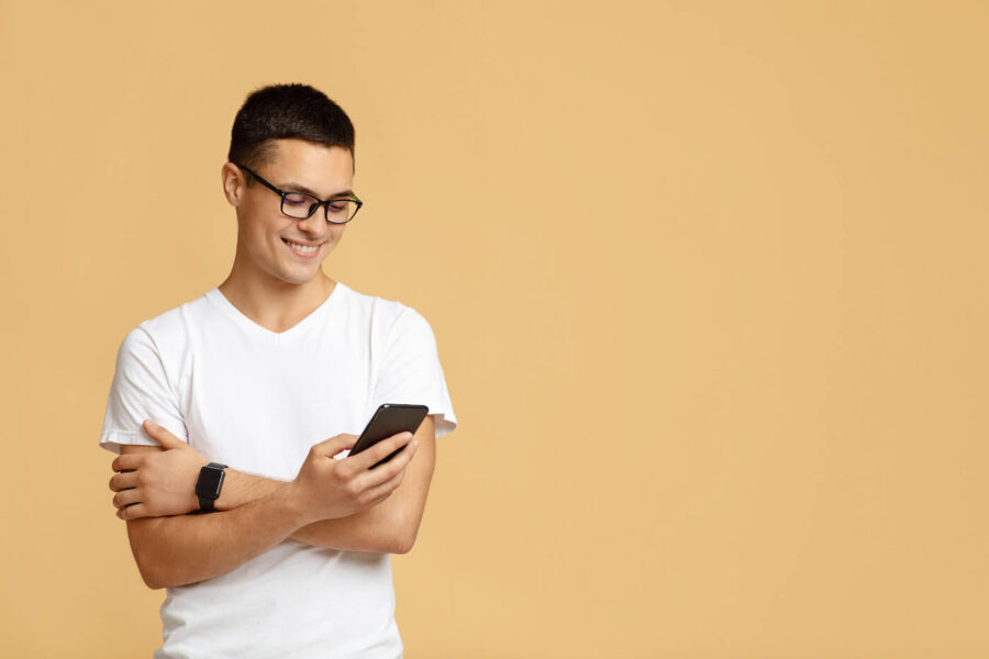 young man in dark glasses and white t-shirt holding phone against orange background