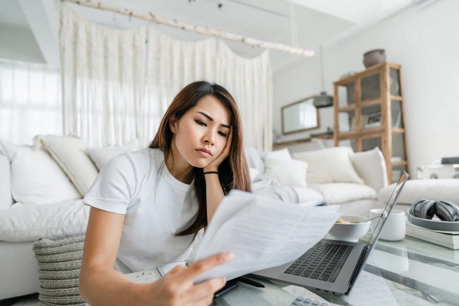 Stressed and worried young Asian woman working from home, handling paperworks and going through her financials