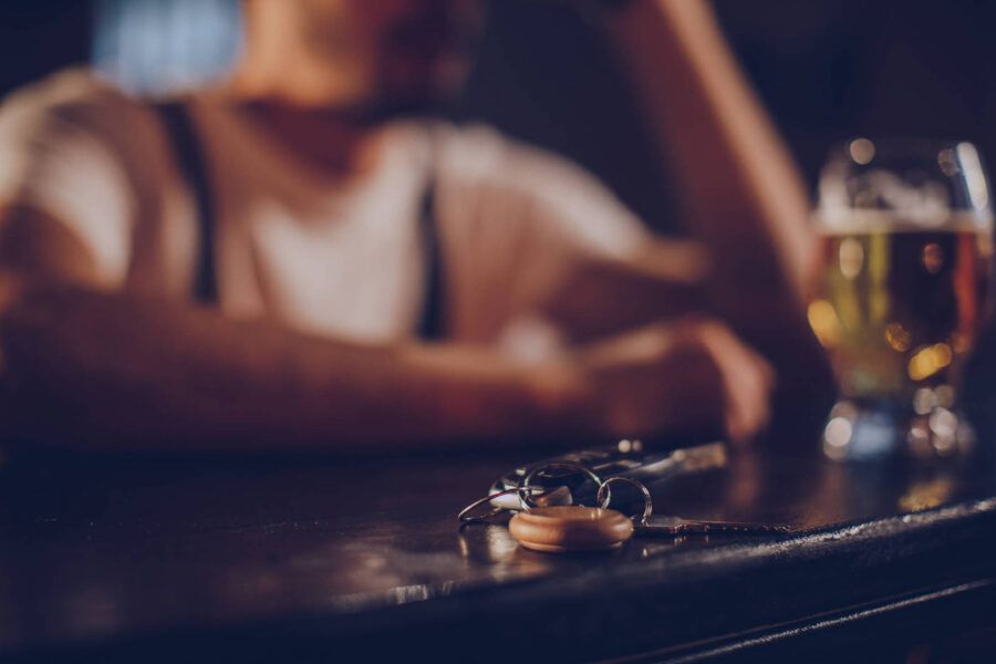 Car keys are sitting at the bar top table while a man wearing a white shirt drinks in the background.