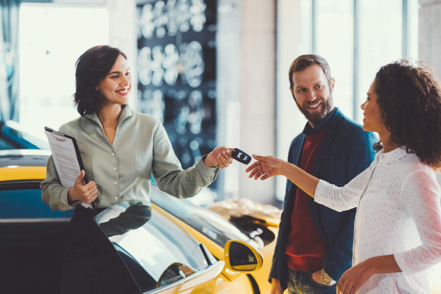 A car salesman smiles while giving a set of car keys to a customer.