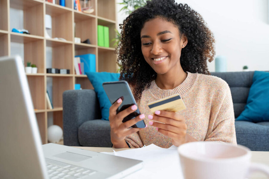 Cheerful young black woman using credit card at home.