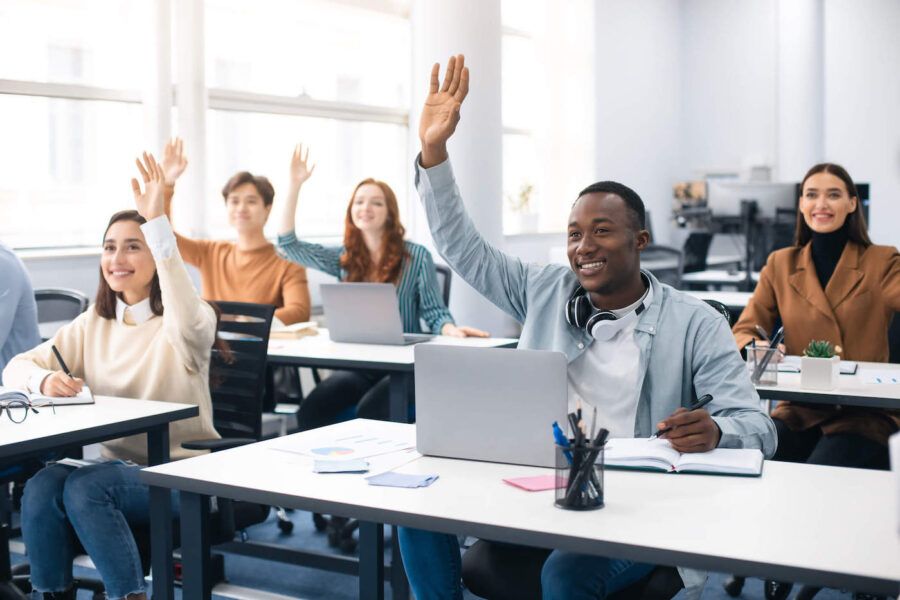 A group of college students smile while raising their hand at the classroom.