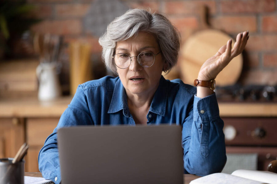 A frustrated middle-aged woman wearing eye glasses and looking at her laptop.