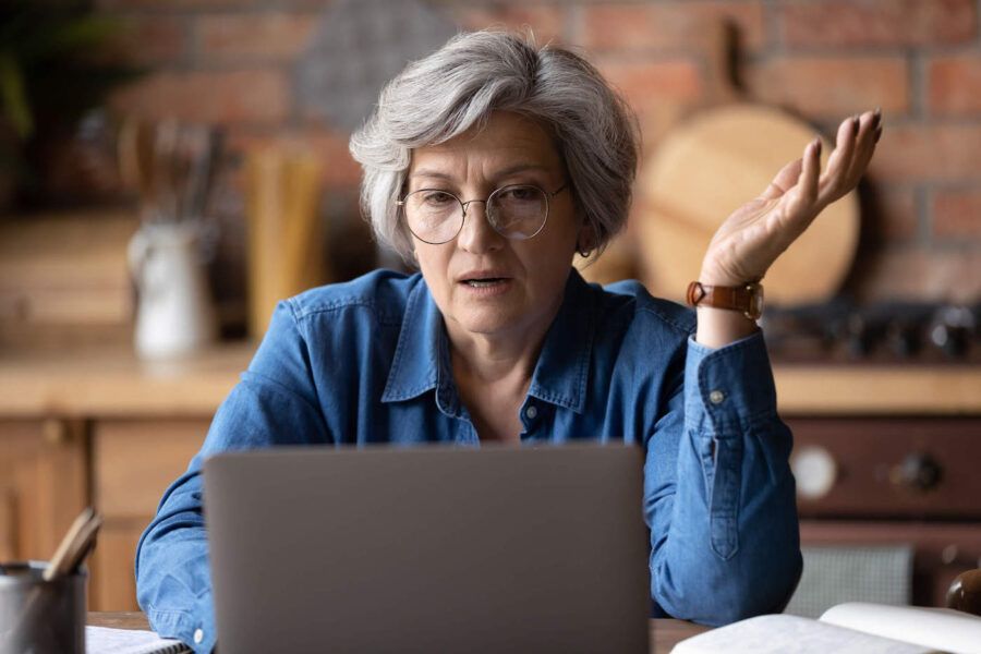 A frustrated middle-aged woman wearing eye glasses and looking at her laptop.