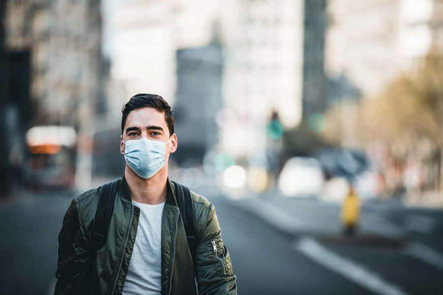 Concept, diseases, viruses, allergies, air pollution. Portrait of young man wearing a protective mask, walking in the city.The image face of a young man wearing a mask to prevent germs, toxic fumes, and dust. Prevention of bacterial infection Corona virus or Covid 19 in the air around the streets and gardens.