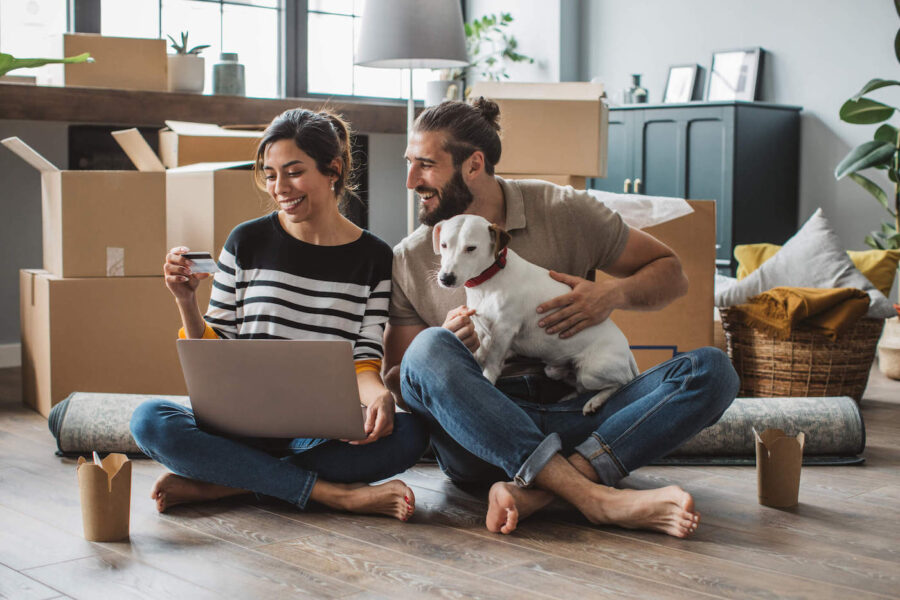 A couple, with their dog, smile together at a credit card while moving into their new home