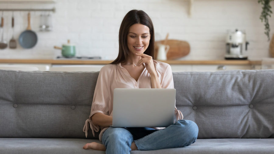 Smiling young woman using laptop, sitting on couch at home