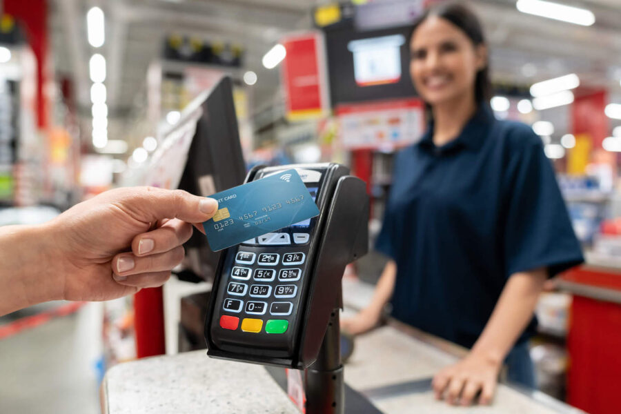 A cashier smiles as a customer's hand is tapping their credit card on the card reader.