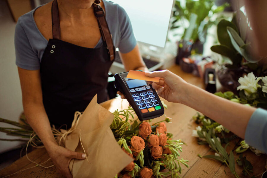 A customer buys flowers by tapping their orange credit card on the card reader.