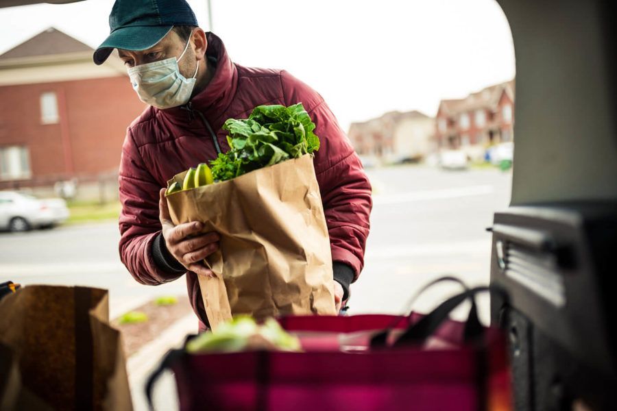 Mature man wearing protection mask, unloading grocery from car trunk