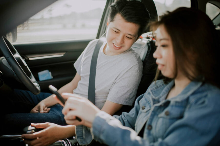 man and woman sitting in a car looking at phone