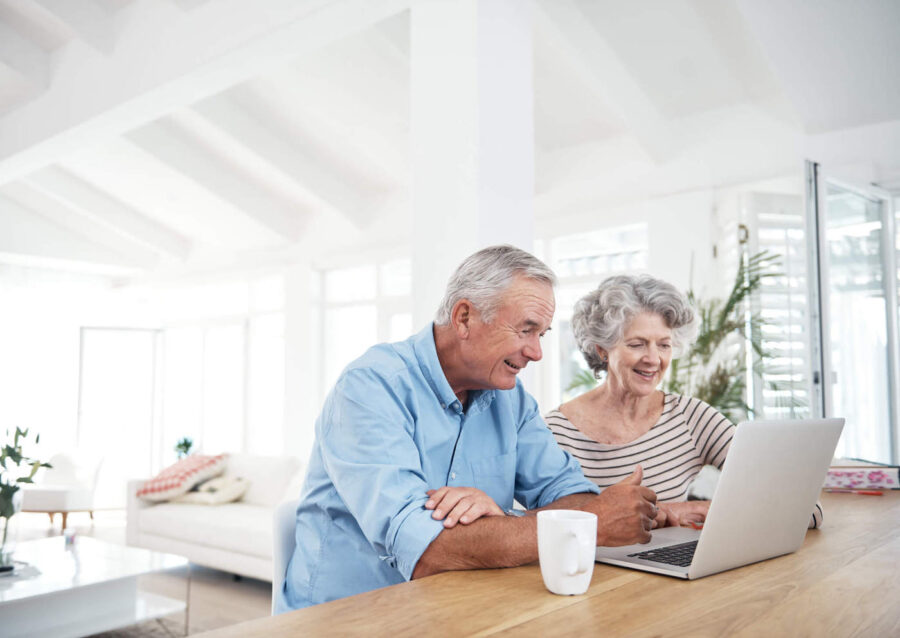 An elderly couple smile while looking at the laptop screen at home.