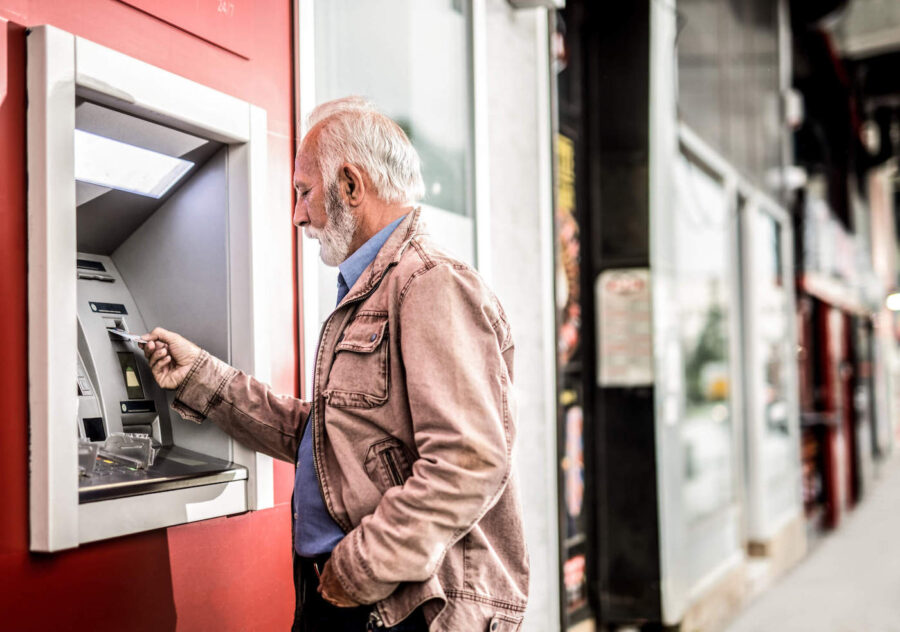 An elderly man wearing a brown jacket puts in his credit card in the ATM.